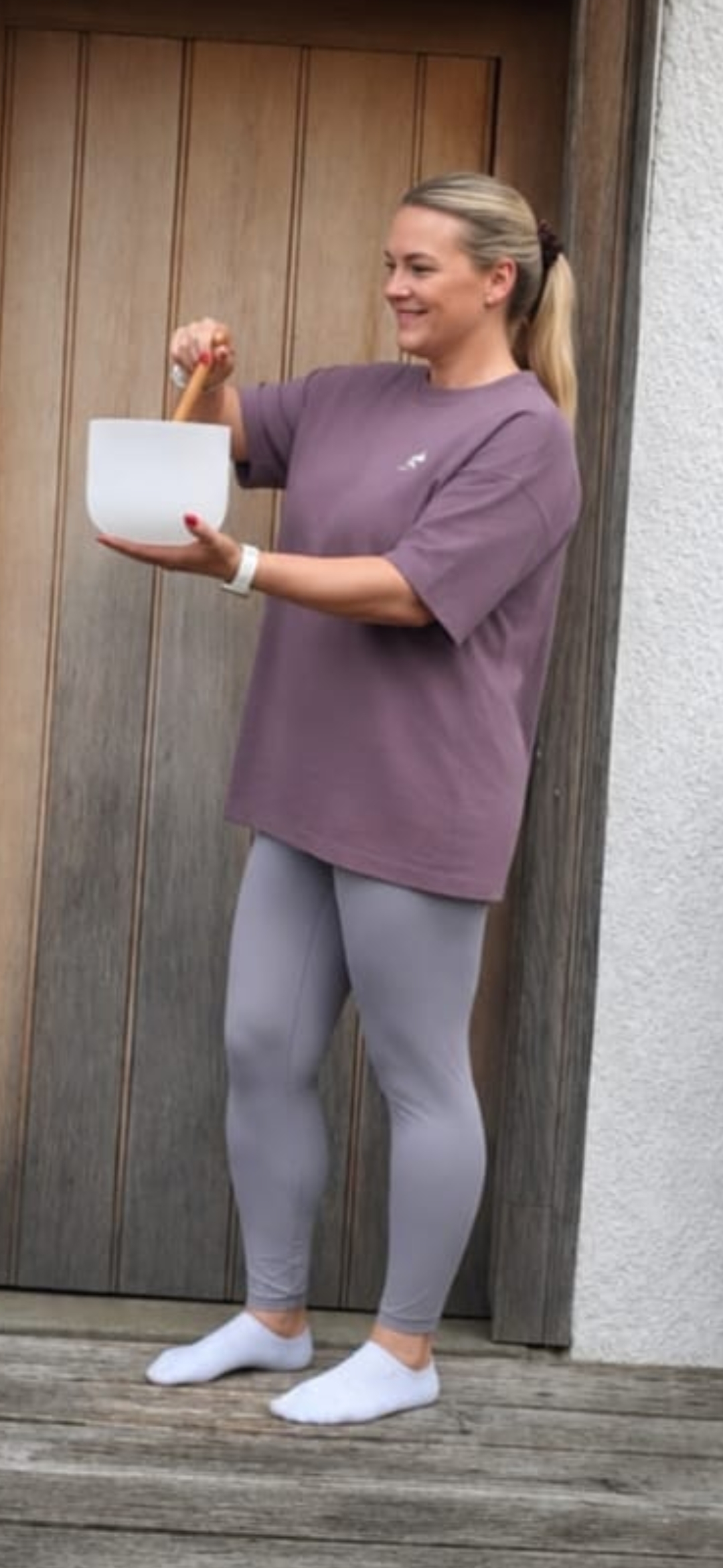 Nicola holding a white singing bowl and mallet before a sound experience